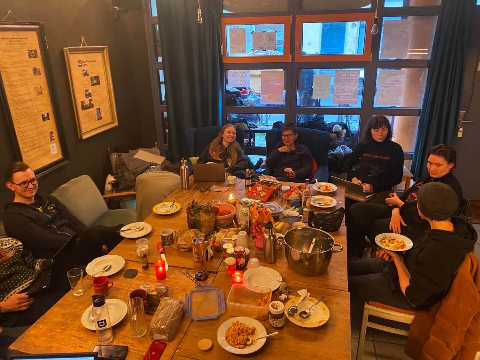 Menschen sitzen um einen mit Essen und Snacks gedeckten Holztisch in gemütlicher Atmosphäre